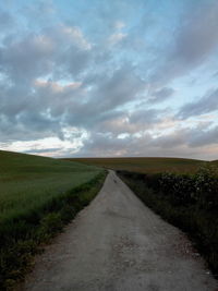 Road passing through field against cloudy sky