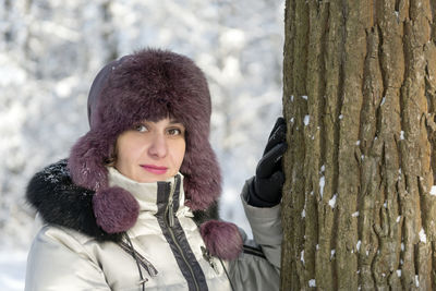 Close-up portrait of young woman by tree trunk in winter