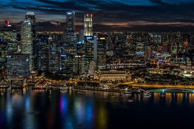 Illuminated buildings by river against sky in city at night