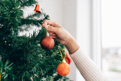 Close up woman's hand touching and decorating a red bauble on the christmas tree in the living room.