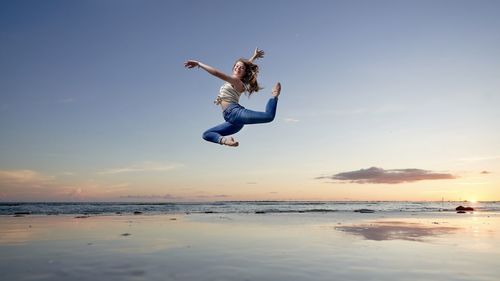 Man jumping at beach against sky during sunset