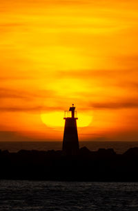 Large sun behind a silhouette lighthouse during a fiery sunset