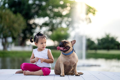 Full length of girl sitting with dog on pier by lake