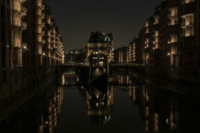 Bridge over canal amidst buildings in city at night