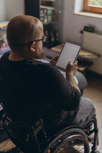 Side view of man using mobile phone while sitting on wheelchair