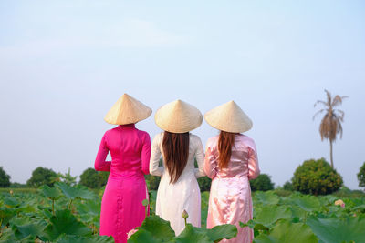 Rear view of women standing on field against sky