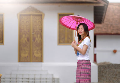 Portrait of woman holding pink umbrella while standing against historic building
