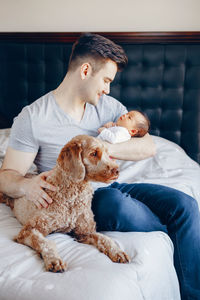 Father carrying baby girl while sitting on bed with dog at home