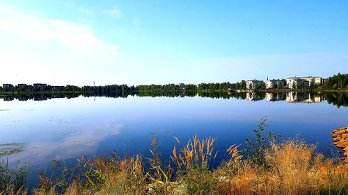 Scenic view of lake by buildings against blue sky