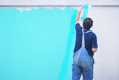 Rear view of painter painting white wall