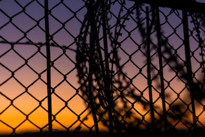 Close-up of chainlink fence against sky during sunset