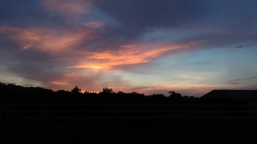 Silhouette trees on field against dramatic sky during sunset