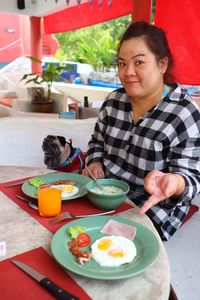 Portrait of smiling woman pointing towards breakfast on table