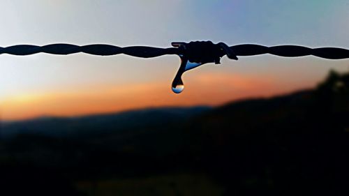 Close-up of water drop on barbed wire against sky during sunset