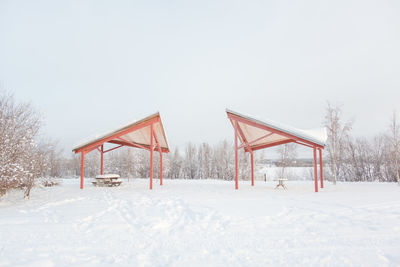 Picnic tables under shed on snow covered field against sky