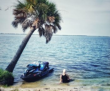 People sitting on palm tree by sea against sky