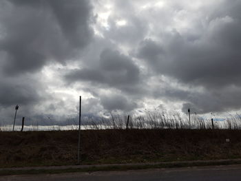 Road passing through field against cloudy sky