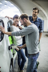 Friends looking at man charging electric car in gas station