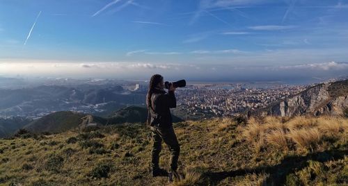 Woman photographing on land against blue sky