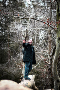 Woman standing by bare trees in forest