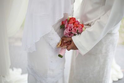 Midsection of bride and groom with bouquet holding hands during wedding ceremony