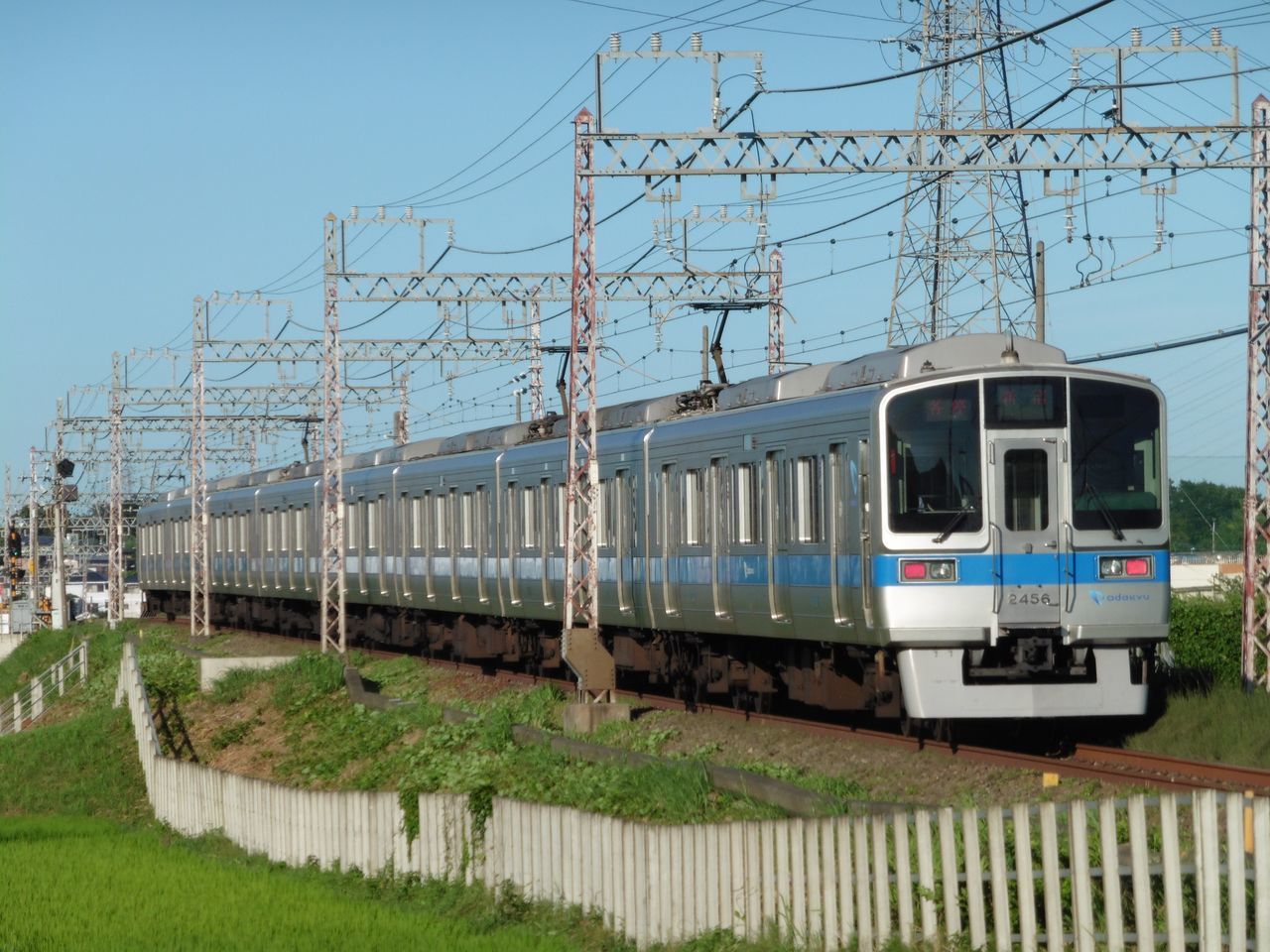 transportation, built structure, architecture, mode of transport, building exterior, clear sky, tree, bare tree, land vehicle, grass, day, car, railroad track, public transportation, sky, outdoors, no people, power line, window, blue