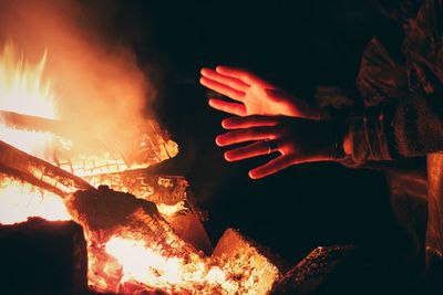 Cropped hands by campfire at night