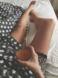 Low section of woman holding coffee cup on bed