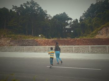 Rear view of couple walking on road against trees