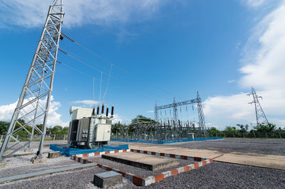 Electricity pylon by road against blue sky