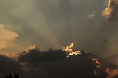 Low angle view of sunlight streaming through clouds