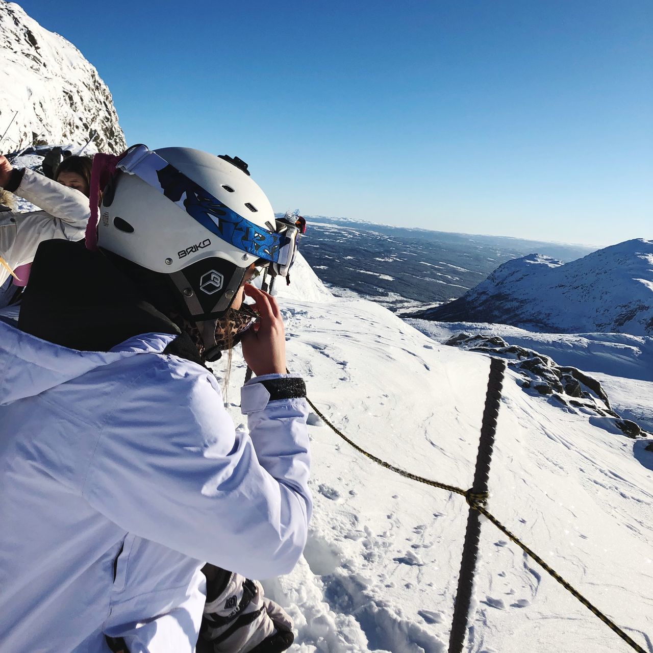 snow, winter, helmet, cold temperature, mountain, adventure, ski goggles, headwear, real people, skiing, sports helmet, leisure activity, one person, sport, mountain range, day, white color, nature, protection, outdoors, lifestyles, sunlight, ski holiday, clear sky, vacations, snowcapped mountain, standing, scenics, warm clothing, beauty in nature, men, extreme sports, snowboarding, ski lift, sky, adult, people