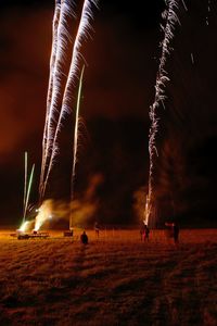 Firework display over field against sky at night