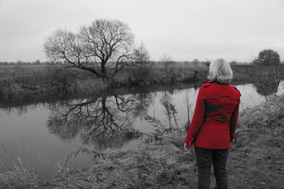 Rear view of man walking by lake against sky during winter