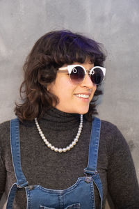 Portrait of young woman wearing sunglasses standing against wall