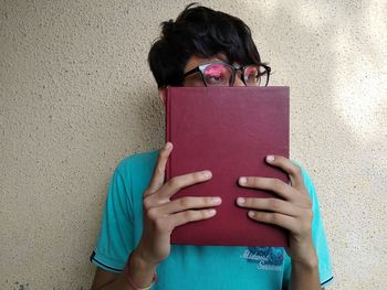 Thoughtful man holding book while standing against wall