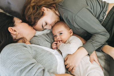 Real family of young mom and two kids of different ages teenager girl and baby boy having fun on bed