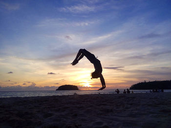 Silhouette man jumping at beach against sky during sunset
