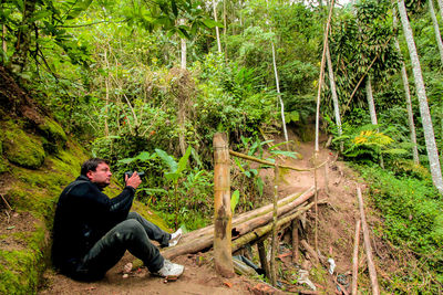 Side view of man photographing through camera while sitting at forest