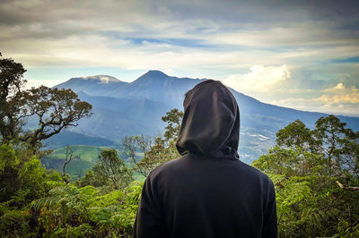 Rear view of man looking at mountains against sky