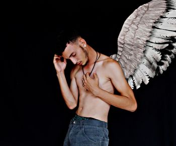 Shirtless man with wings against black background