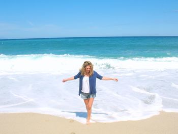 Full length of young woman standing with arms outstretched at beach