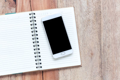 Directly above shot of smart phone on spiral notebook at wooden table