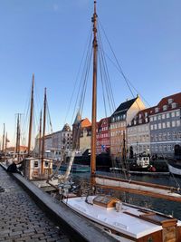 Sailboats moored at harbor by buildings against sky