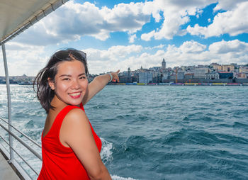 Portrait of smiling woman pointing while standing by railing in nautical vessel on sea