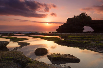 Rocks on sea shore against sky during sunset