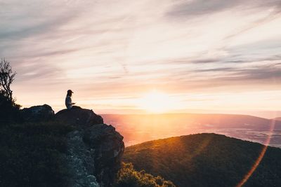 Silhouette woman sitting on rock against sky during sunset