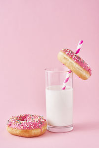 Donuts decorated with icing and sprinkle and glass of milk on pink background