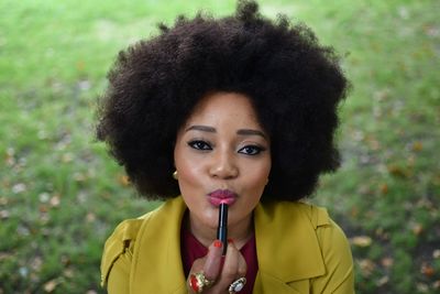 High angle portrait of woman applying lipstick at field