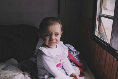 Portrait of cute baby girl crying while sitting on bed at home